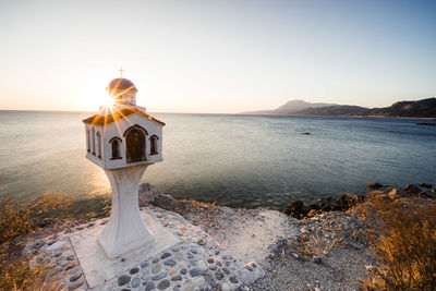 Religious built structure by sea against clear sky during sunset