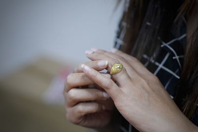 Midsection of woman wearing gold finger ring at home