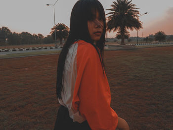 Woman standing by palm trees on land against sunset sky