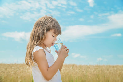 Young woman drinking water against sky