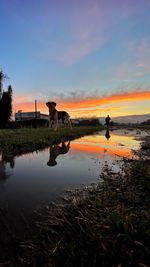 Men on field by lake against sky during sunset