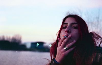 Portrait of young woman smoking cigarette against sky