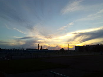 Silhouette factory against sky at sunset