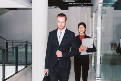 Portrait of businessman with secretary standing in building corridor
