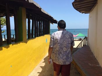 Rear view of man walking on street leading towards sea