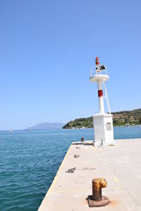 Lighthouse by sea against clear blue sky