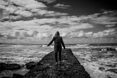 Rear view of person wearing hoodie standing by sea against sky