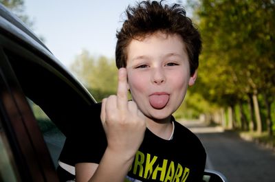 Portrait of boy sticking out tongue while showing middle finger in car