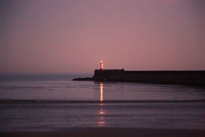 Lighthouse by sea against sky at sunset