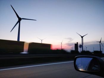 Wind turbines on street against sky during sunset