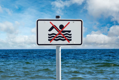 Close-up of road sign by sea against sky