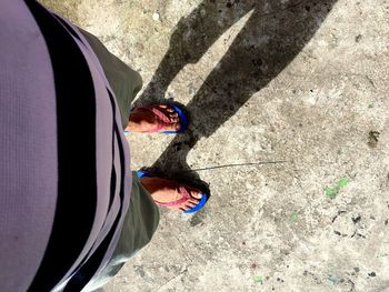 Low section of man standing on footpath during sunny day