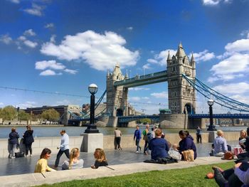 People on promenade by thames river against tower bridge