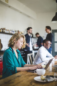 Serious female it hacker using laptop while colleagues talking in background at creative workplace