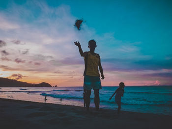 Rear view of couple standing at beach during sunset