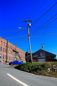 Road by buildings against blue sky