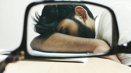 Young man sleeping at desk seen through eyeglasses in classroom