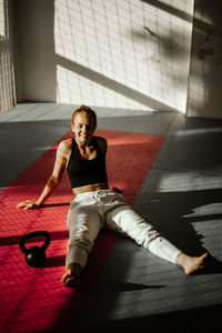 Smiling young woman by barbell relaxing in gym