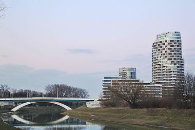 Arch bridge over river against buildings in city against sky