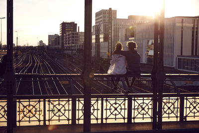 Germany, munich, young couple sitting on bridge, enjoying sunset