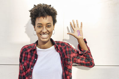 Portrait of smiling young woman standing against wall