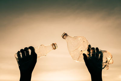 Silhouette people holding bottle against sky during sunset