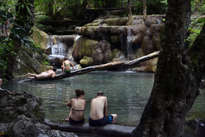 Rear view of two people sitting on riverbank