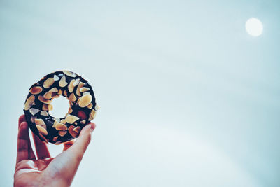 Close-up of hand holding donut against sky