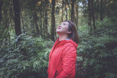 Side view of smiling mid adult woman looking up while standing in forest