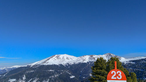 Road sign on snowcapped mountain against blue sky