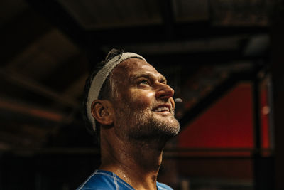 Smiling male athlete wearing headband while contemplating at sports court