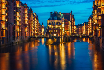 View of illuminated building by canal at dusk
