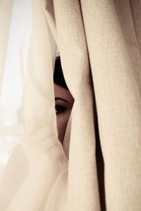 Close-up of young woman hiding behind curtain