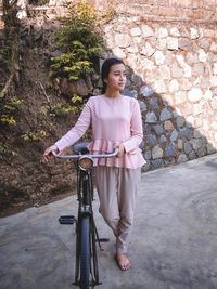 Portrait of woman with bicycle standing against wall