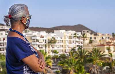 Side view of senior woman looking away standing against cityscape