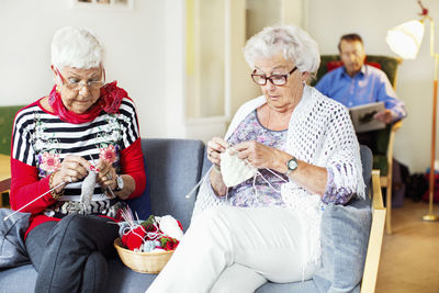 Senior women knitting while man reading book in background at nursing home