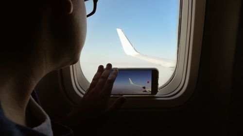 Woman photographing aircraft wing through smart phone while traveling in airplane