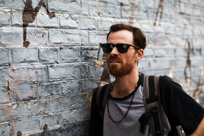 Man wearing sunglasses white standing by brick wall