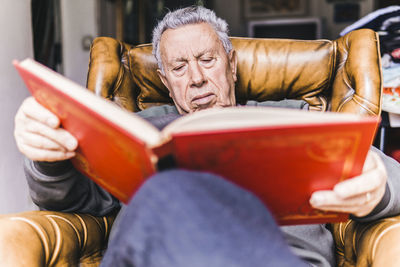 Low angle view of man reading book while relaxing on armchair at home