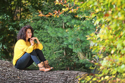 Young woman using mobile phone while sitting on tree