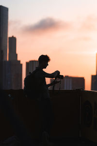 Rear view of man photographing against sky during sunset