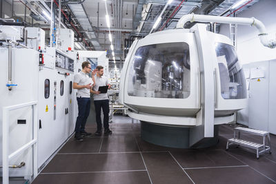 Two men talking at machine in factory shop floor