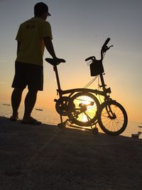 Rear view of man standing by bicycle at beach during sunset