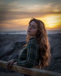 Young woman looking away at beach against sky during sunset