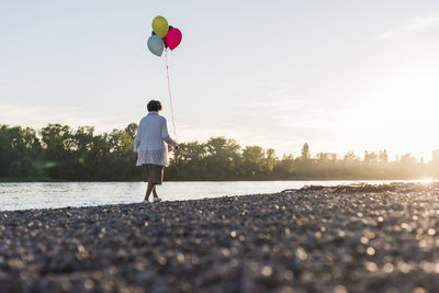 Back view of senior woman with balloons strolling at riverside