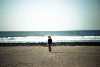 Woman standing at beach against clear sky