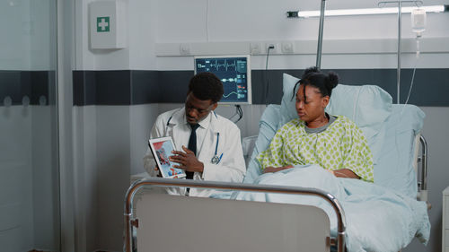 Doctor showing test result on tablet pc to patient in ward at hospital