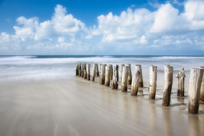 Wooden posts on beach against sky