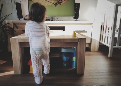 Rear view of girl standing on table at home