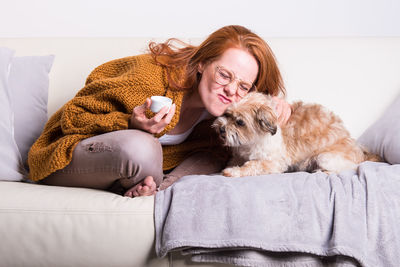 Woman playing with dog while sitting on sofa at home